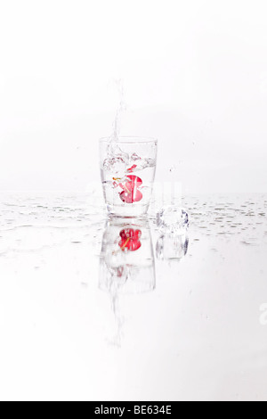 Cocktail cherry falling into a water glass with ice cubes Stock Photo