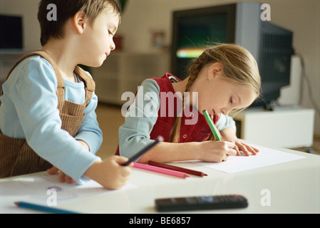 Siblings drawing with colored pencils, little boy pausing to look over sister's shoulder Stock Photo