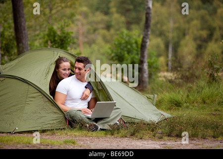 A couple using a computer outside a tent on a camping trip Stock Photo