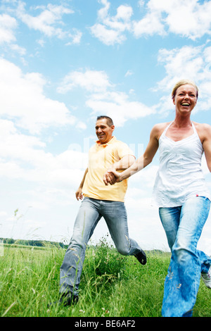 Couple running across a meadow, holding hands Stock Photo