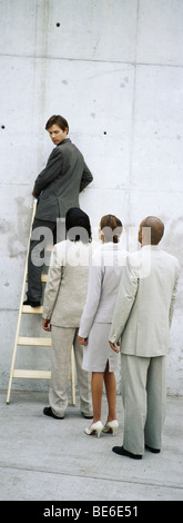 Businessman climbing ladder, looking over shoulder at professionals lined up behind him Stock Photo