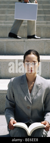 Businesswoman sitting outdoors holding book, eyes closed Stock Photo