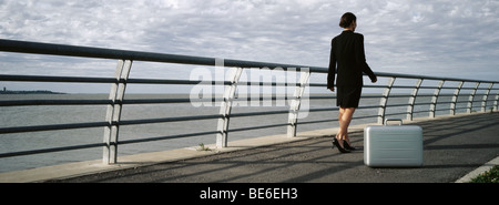 Briefcase set on ground near waterfront railing, businesswoman walking away