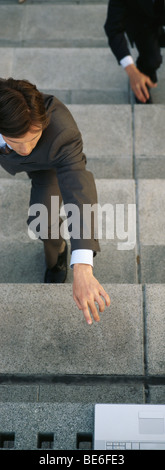 Businessmen crouching on steps reaching for laptop computer set at top of stairs Stock Photo