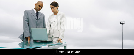 Business associates standing together outdoors, looking at laptop computer Stock Photo