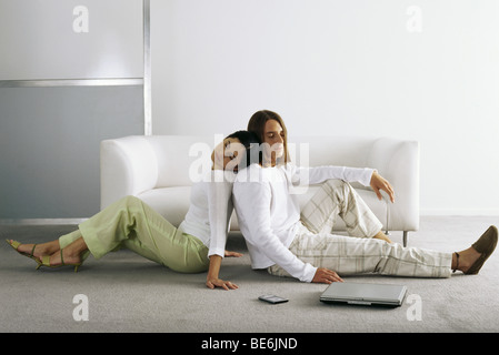 Couple sitting back to back on floor, woman resting head on man's shoulder Stock Photo