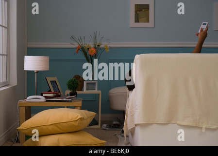 Person reclining on sofa controlling air conditioner with remote control, rear view Stock Photo