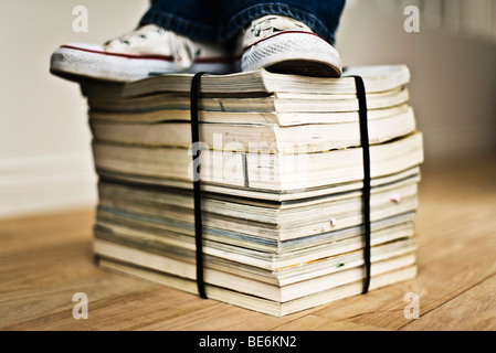 Person standing on top of bound stack of paper catalogs and magazines Stock Photo