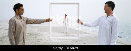 Woman on beach seen through picture frame held up by two men Stock Photo