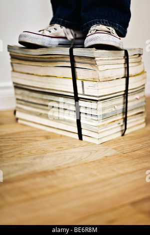 Person standing on top of bound stack of books and magazines Stock Photo