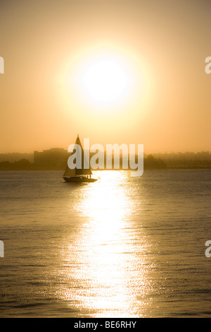 A sailboat on the Pacific Ocean with the sun setting behind it in San Diego, California. Stock Photo