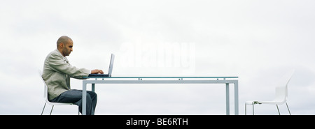 Man sitting outdoors using laptop computer Stock Photo