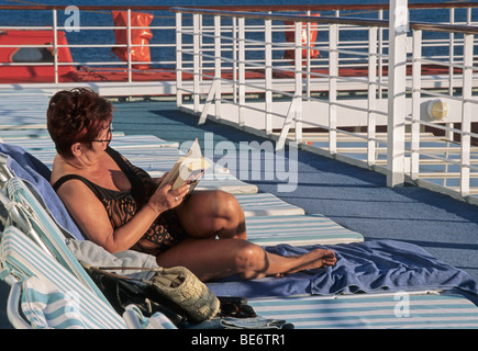 lady reading a book on a sunbed on the exterior deck of a cruise liner Stock Photo