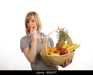 Young woman holding a fruit basket and biting into a red apple Stock Photo
