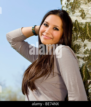 Young woman, 20, leaning against a tree, half portrait Stock Photo