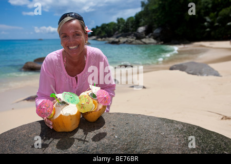 A woman in a pink tunic reaches for two decorated coconuts filled with drinks, island Mahe, Seychelles, Indian Ocean, Africa Stock Photo