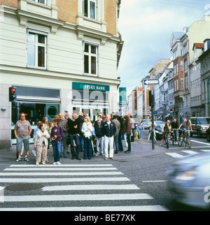 Pedestrians and cyclists waiting at traffic lights and zebra crossing near a Jyske Bank in a street in Copenhagen Denmark Stock Photo
