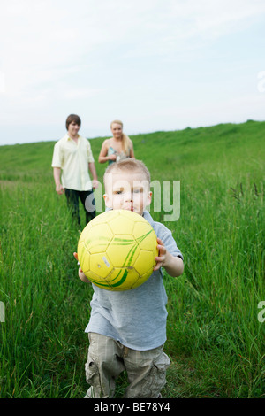 Young parents watching their son running away with a ball Stock Photo