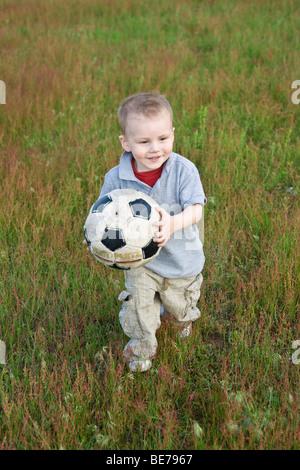 Two-year-old boy holding a ball, running across a lawn Stock Photo