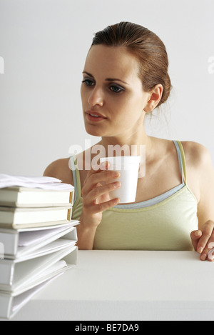 Woman on break looking with curiosity at stack of books and binders Stock Photo