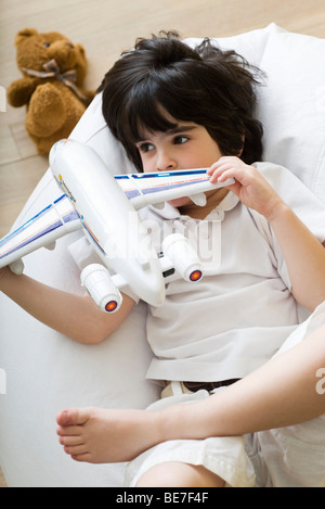 Little boy lying on beanbag chair, playing with toy airplane Stock Photo