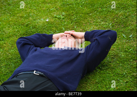 man asleep on grass with hands clasped on head UK Stock Photo
