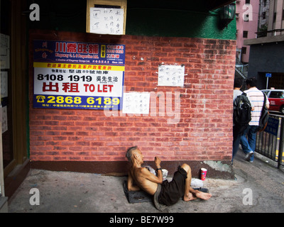 Hong Kong. Tramp  on Caine Road, a typical busy middleclass neighbourhood  On the wall ads from a property agent. Stock Photo