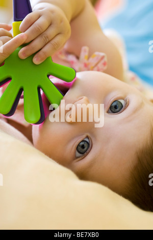 Infant girl chewing on plastic toy, looking at camera Stock Photo