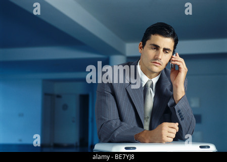 Businessman sitting with briefcase on lap in empty office using cell phone Stock Photo