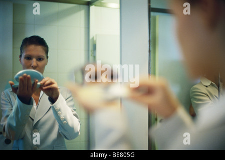 Woman holding powder compact putting on makeup, over shoulder view Stock Photo