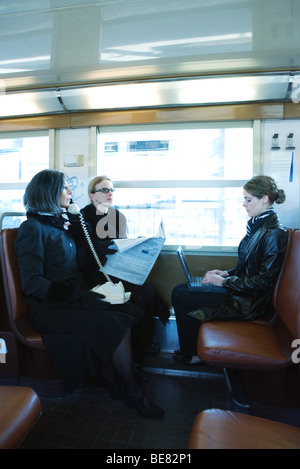 Commuters on train, one using landline phone, another using laptop computer Stock Photo