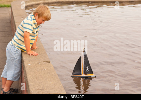 A small boy ( model released ) sailing his toy boat at the boating lake in Aldeburgh , Suffolk , Uk Stock Photo