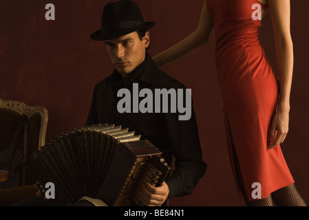 Man sitting, playing accordion, woman standing beside him, cropped view Stock Photo