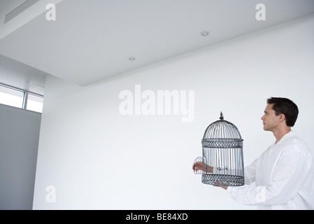 Man holding empty bird cage with open door, side view Stock Photo