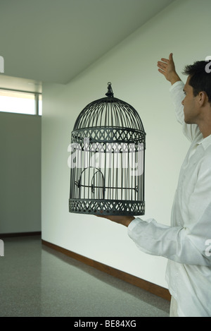 Man holding empty bird cage with open door, arm raised, side view Stock Photo