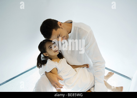 Father holding daughter on lap, leaning head toward her face Stock Photo