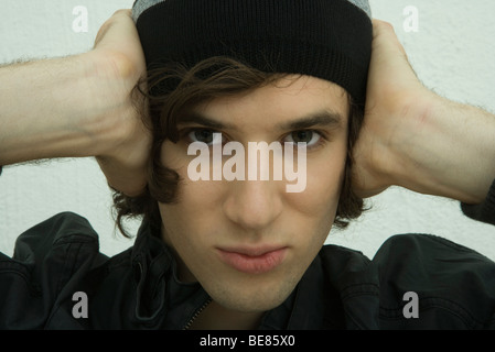 Young man holding hands over ears, staring at camera Stock Photo