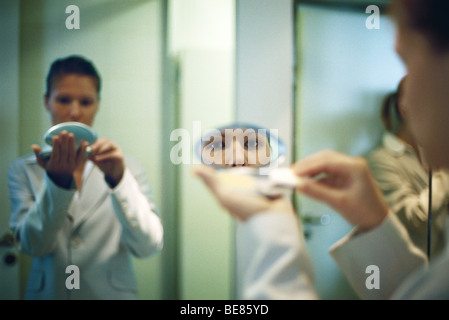 Woman holding powder compact putting on makeup, looking at camera in reflection in mirror Stock Photo
