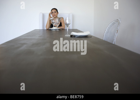 Woman sitting alone at table set for two, holding head Stock Photo