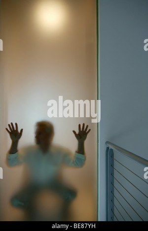 Man crouching behind window, hands pressed against glass Stock Photo