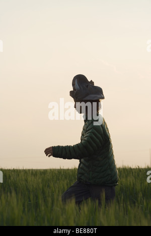 Preteen girl walking through field of tall grass, animal mask on head, side view Stock Photo