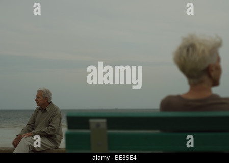Senior man sitting on bench, looking away, senior woman in foreground Stock Photo