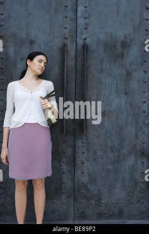 Woman standing beside double doors, eyes closed, frowning Stock Photo