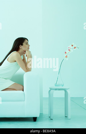 Woman sitting on sofa, admiring orchid Stock Photo