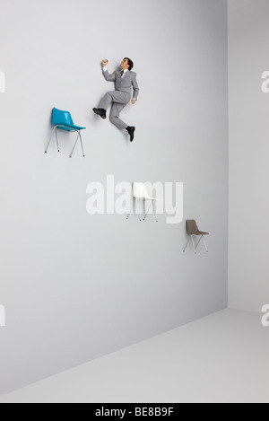 Businessman leaping midair from chair to chair Stock Photo