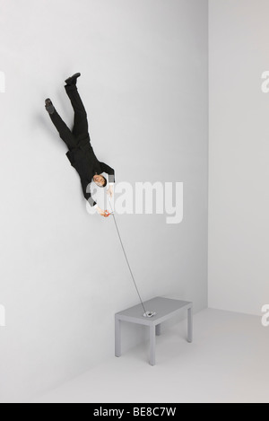 Businessman floating upside down holding landline phone, cutting cord with scissors Stock Photo