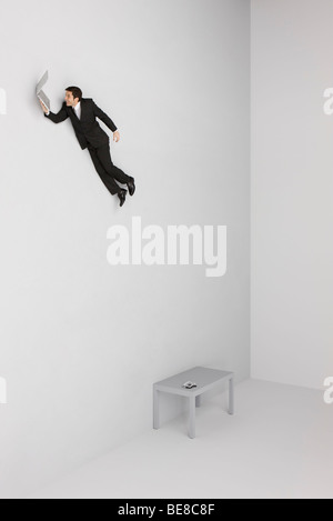 Businessman holding laptop computer flying away from desk below Stock Photo