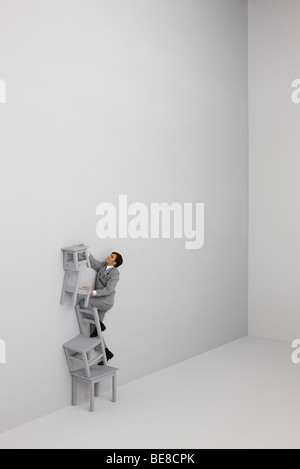 Businessman climbing ladder made of stacked chairs Stock Photo