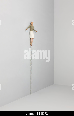 Woman balanced atop stack of water bottles, arms out Stock Photo