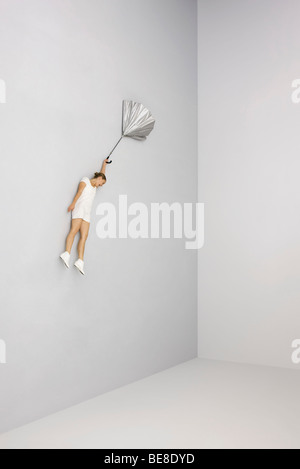 Woman holding umbrella blown inside out, floating in midair Stock Photo